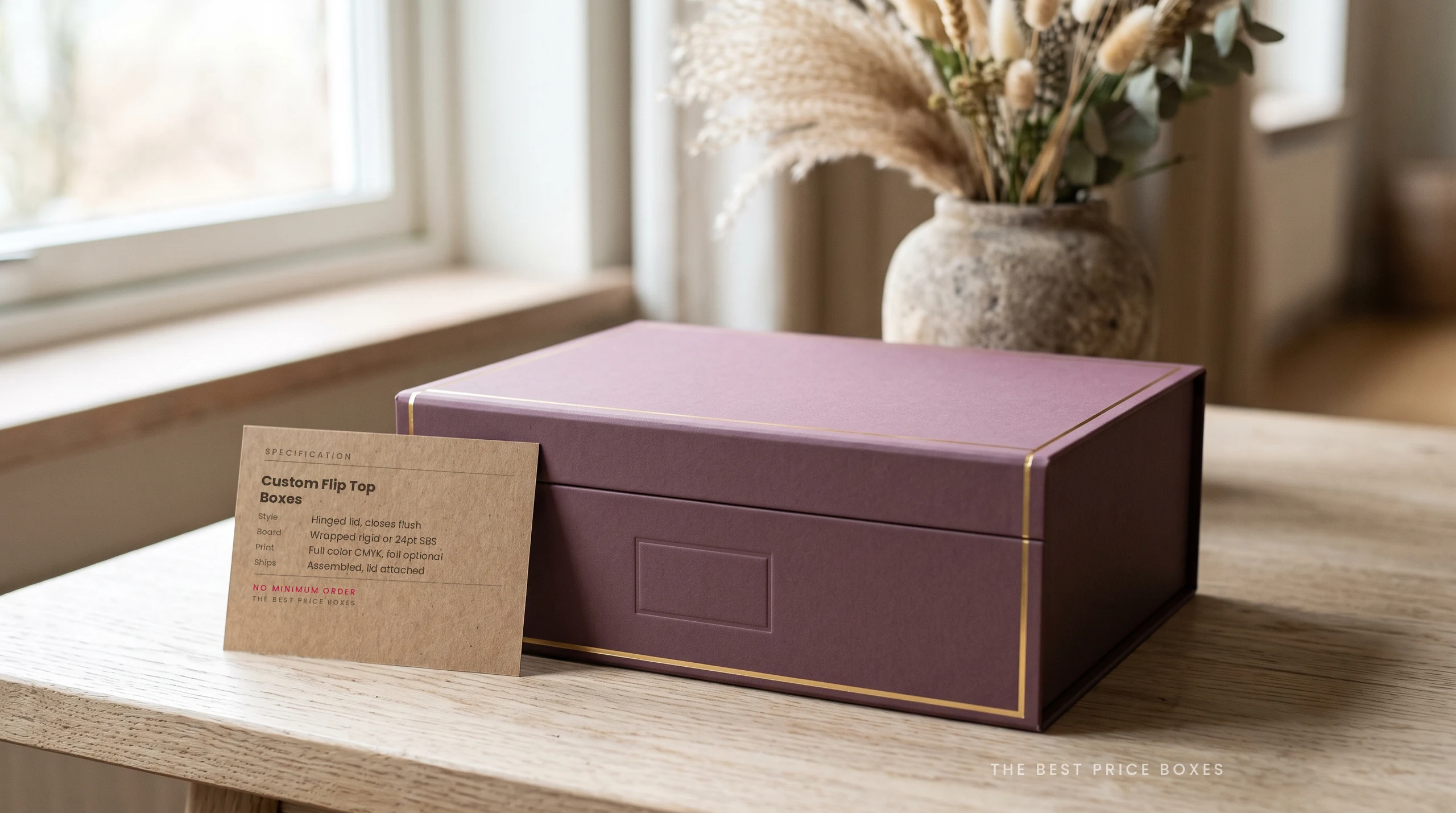 Custom flip top box in muted plum with a brass foil edge line and a lid hinged at the back, next to a kraft spec card listing board, print and shipping options.
