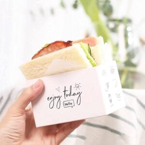 Custom toast packaging box held in one hand, a printed carton sized to hold a filled sandwich.