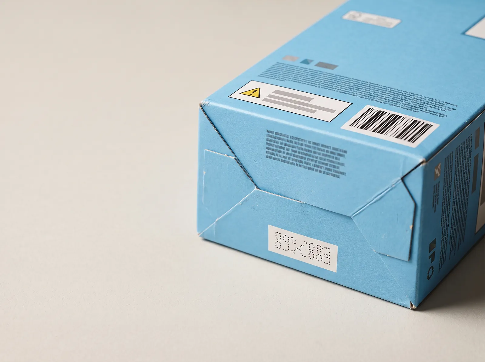 Bottom of a blue toy carton showing a warning label panel, a barcode and a printed batch tracking code