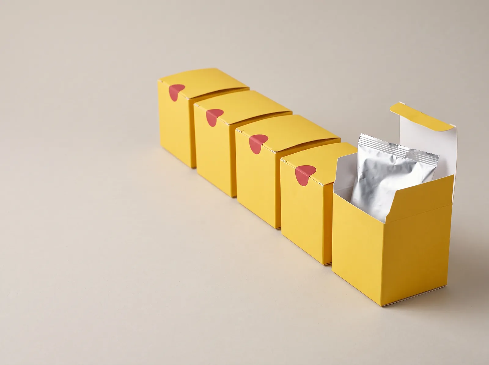 Row of identical sealed yellow blind boxes, the last one open to show a foil bag hiding the toy inside